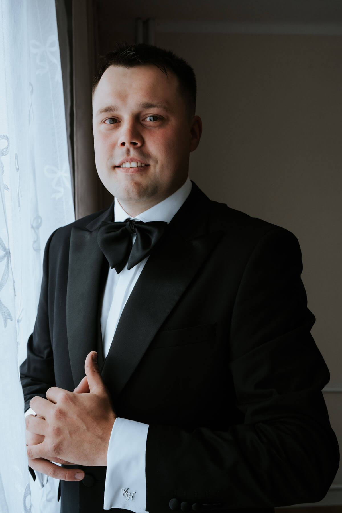 Konrad, Pan Młody, w eleganckim garniturze przy oknie przed ślubem